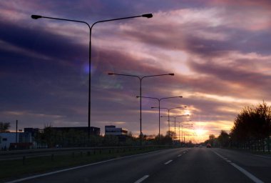 Arka planda lambalar bir satır ile gün batımında Karayolu. Şehirden akşam trafiği. Karayolu taşımacılığı.