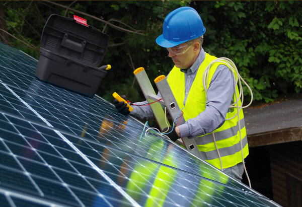 Installation and commissioning of solar panels. Renewable energy in a private home. Worker with electrical appliances on the roof.