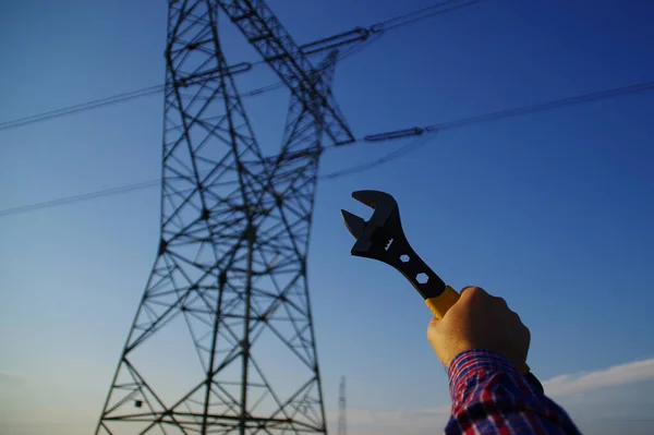 Industry and power line maintenance concept. Wrench in hand with silhouette of electric pylon in background. Energy network service.