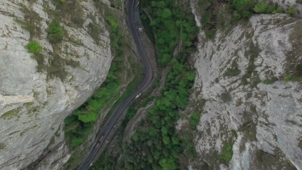 Aerial view flying over old patched two lane forest and rocks road with car moving green trees of dense woods growing both sides — Stock Video