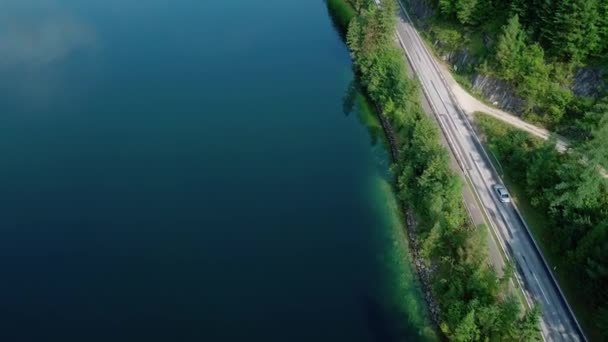 Letecký pohled na stříbrné auto přes les a jezero na venkovské silnici, pohled shora dolů — Stock video