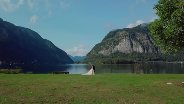 Μέρα του γάμου. νεόνυμφοι γαμήλιο ζευγάρι στέκονται μαζί κοντά στη γαλάζια λίμνη και το βουνό — Αρχείο Βίντεο