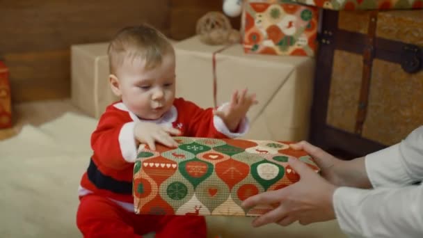 Erstaunliche Blick der Mutter, die ihrem aufgeregten netten kleinen Jungen oder Mädchen ein Geschenk gibt, das ihre Hände in der Nähe eines geschmückten Weihnachtsbaums und Geschenks klatscht — Stockvideo