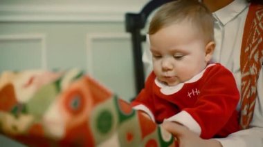 Bir genç kız baktı şaşırtıcı bir çocuk bir şekilde dekore edilmiş Noel ağacı ve hediye Anne kucağında oturan bir çocuk için bir hediye verir. Yakın çekim