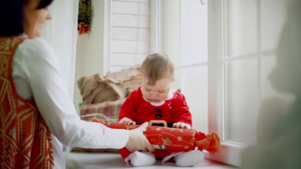 Aparência incrível de menina ou menino em um terno de Natal sentado na janela e recebendo um presente da mãe perto de uma árvore de Natal decorada e presente. Fechar — Vídeo de Stock