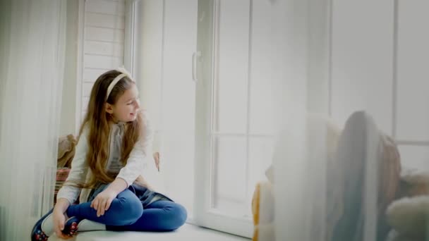 Niña linda sentada en el alféizar de la ventana, mirando hacia fuera — Vídeos de Stock