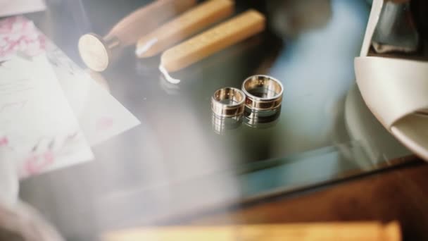 Dos anillos de boda de oro acostados en una mesa con decoraciones que brillan con luz de cerca macro. Transfusión de luz en anillos — Vídeos de Stock