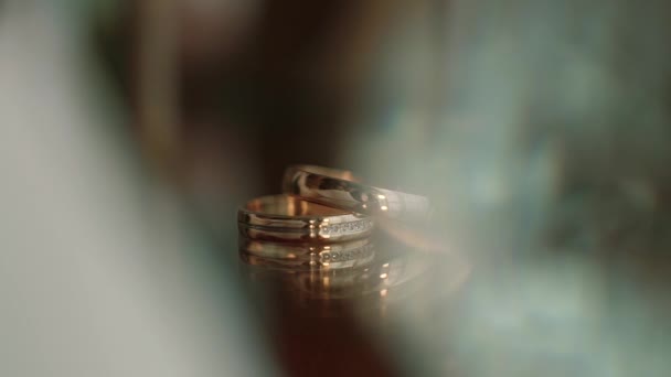 Due fedi nuziali d'oro distese su un tavolo con decorazioni brillanti di luce macro primo piano. Trasfusione di luce sugli anelli.. Close up — Video Stock