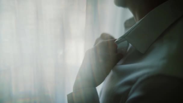 Мужчина застегивает белую рубашку, стоя перед ярким окном, бизнесом, модой и концепцией одежды - крупным планом мужской одежды — стоковое видео