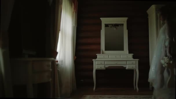 Bride in a white silk dressing gown walks along the panoramic window in wood house — Stock Video