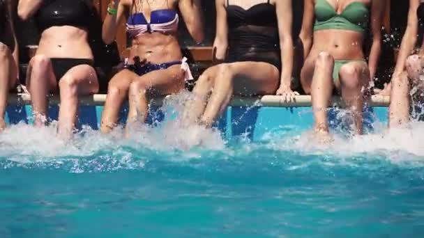 Amigos em uma festa de verão meninas com bebidas coloridas fazer um respingo pernas na água sentado na piscina. Motim lento — Vídeo de Stock