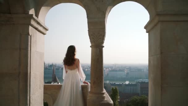 Uma jovem muito bonita ou noiva em um vestido branco, ficar na varanda do castelo velho, e olha para a cidade Budapeste. de perto — Vídeo de Stock