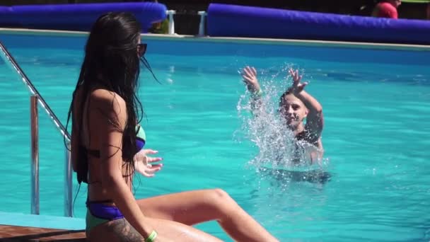 Glad rolig kärleksfull grupp unga kvinna i en sexig bikini sitter i poolen, en ung man strilar vatten flickan, Slowmotion — Stockvideo