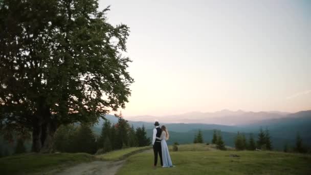 Pareja de pie juntos yver la puesta de sol en la cima de la montaña y disfrutar — Vídeos de Stock