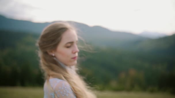 Retrato de mujer joven con el pelo soplando en el viento mirando el atardecer en la montaña. Moción lenta — Vídeos de Stock