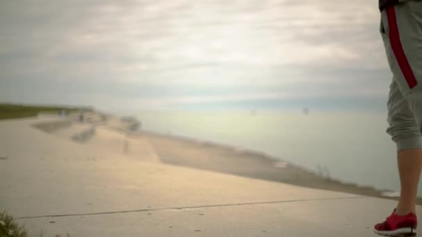 Un giovane atletico gambe che corre sullo sfondo della città e del lago, fotocamera vista laterale anteriore, rallentatore — Video Stock