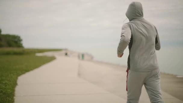 Молодой спортсмен бежит на фоне города и озера, вид, замедленное движение, камера сбоку — стоковое видео