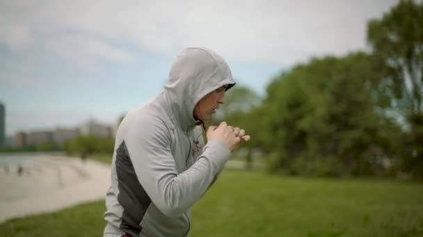 Молодой спортсмен тренирует бокс на фоне города и озера, вращает камеру, замедленное движение — стоковое видео