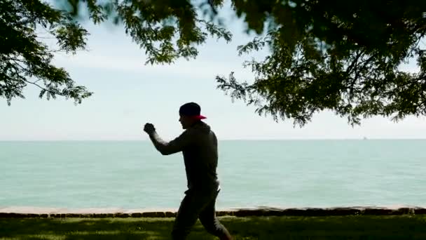 Silhouette un joven deportista, activamente dedicado a los deportes, crossfit, boxeo, kickboxing en la orilla del lago — Vídeo de stock