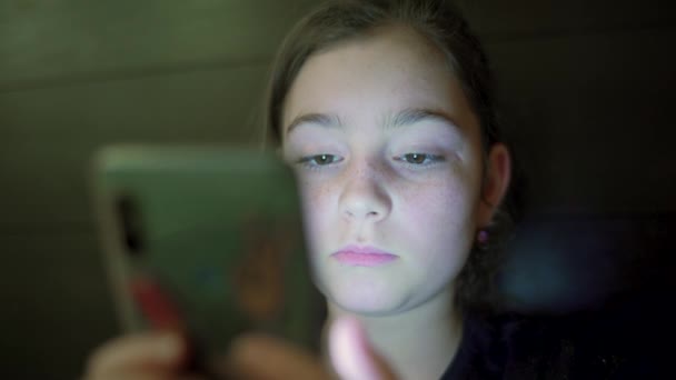 Foto nocturna de niños adolescente cara de niña navegando teléfono inteligente con reflejo de luz en él. De cerca. — Vídeos de Stock