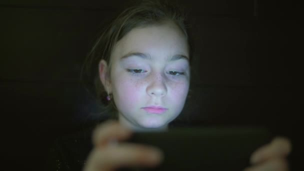 Noche de fotos de niños adolescente cara de la muchacha de navegación tableta PC o teléfono inteligente con reflejo de luz en él — Vídeo de stock