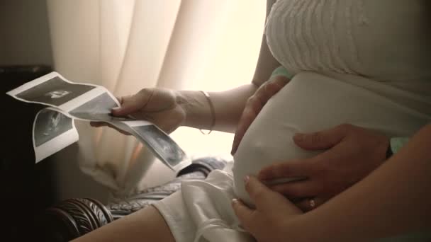 Ζευγάρι που κοιτάζει την υπερηχογραφική σάρωση του μωρού στον καναπέ. Αργή κίνηση — Αρχείο Βίντεο