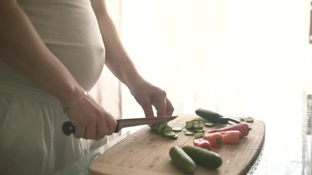 Kobieta w ciąży tnie warzywa brzuch kobiety w ciąży i ręce wyostrzenie nóż kuchenny na stole. — Wideo stockowe