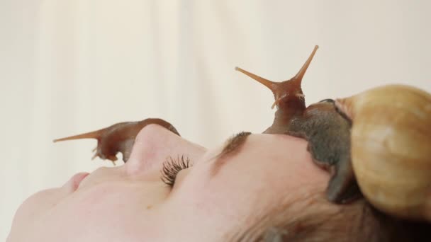 Spa. Deux gros escargots sur le visage. Jeune femme au spa reçoit un massage du visage avec des escargots Achatina. Les escargots mangent la peau morte des produits. Au final, il laisse la peau lisse et fraîche — Video