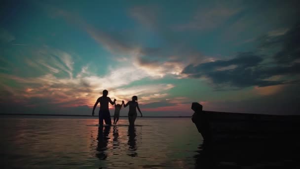 Famil gå på en sjö vid solnedgången. Silhuetter av lite barn och föräldrar tid tillsammans nästa, springa och leka. Slow motion — Stockvideo