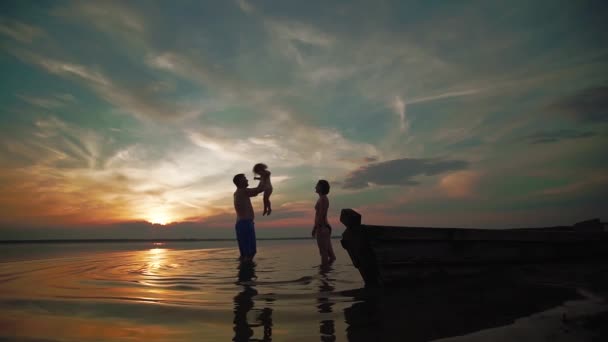 Famil spelen op een meer bij zonsondergang. Silhouetten van een kleine kinderen en ouders tijd samen volgende, rennen en spelen. Slow Motion — Stockvideo