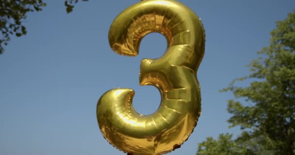 Gold foil number 3 celebration balloon on a blue sky — Stock Video