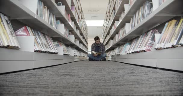 Studentka siedzi na podłodze w bibliotece, czytając książkę. Kształt pionowy, midle vqiew — Wideo stockowe