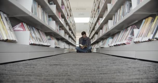 Étudiant assis sur le sol à la bibliothèque, livre de lecture. Forme verticale, milieu vqiew — Video