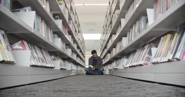 Student vysoké školy, který sedí na podlaze v knihovně, čte knihu. — Stock video