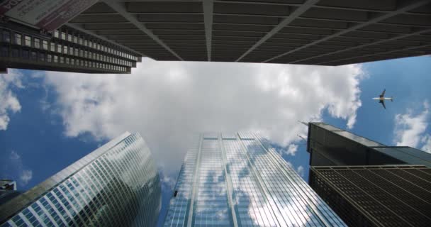 Olhando para arranha-céus edifícios de negócios em dowmtown eo avião voa sobre as nuvens da cidade rolando no céu e reflexões sobre o vidro — Vídeo de Stock