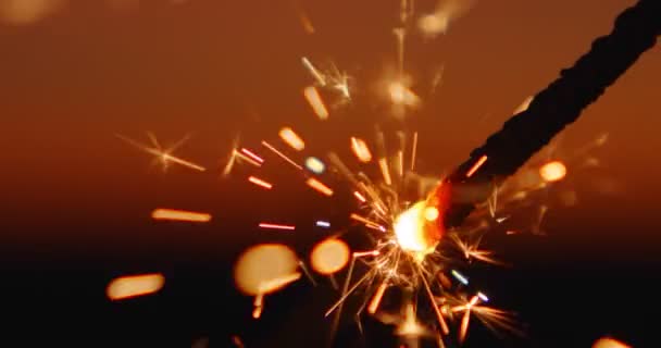 Una varita ardiente brillante de fuego bengalí en cámara lenta contra el fondo del asombroso cielo bokeh al atardecer del día. Las luces naranjas caen por todos lados. Patrón de Navidad y Feliz Año Nuevo. De cerca. — Vídeos de Stock