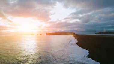 Hava aracı görüntüsü Reynisfjara Sahili 'nde gün batımını, siyah kum plajını ve kaya oluşumlarını gösteriyor Reynisfjara, Vik İzlanda