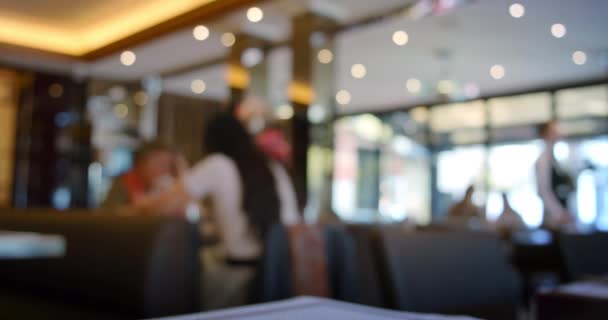 Vídeo borroso del interior de un restaurante con iluminación brillante. Restaurante desenfocado. Los visitantes en la mesa y le da un menú y va a tomar algo — Vídeo de stock