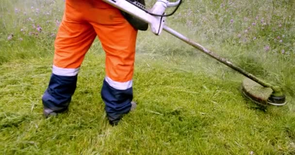 穿着橙色工作服的工人在草坪上用汽油割草机割草，用慢动作的斜视 — 图库视频影像