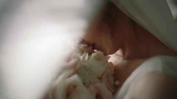 Утро невесты в белом пеньюаре держит в руках свадебный букет роз и нюхает его. Закрыть . — стоковое видео