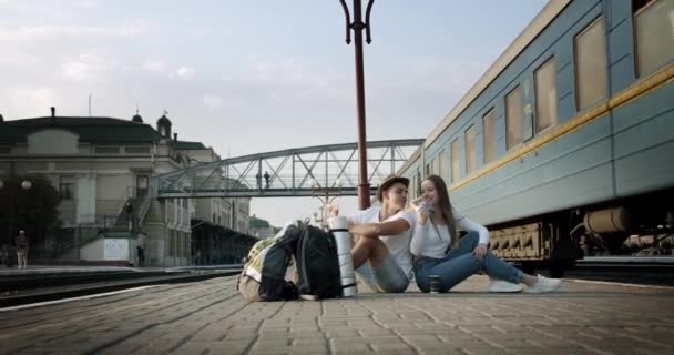 Randi fiatal pár Együtt ülnek az állomás peronján, és esznek szendvicset együtt, egy vonat halad el mellettük Jól érzik magukat.