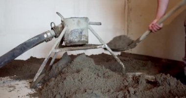 İnşaat alanındaki inşaat alanındaki çelik çitlerin üzerine kürek çimento döken bir inşaat işçisi. Ağır çekimde yakın çekim