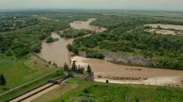 Luchtdrone zicht. Rivierwater stroomt naar beneden met een met water gevulde dam na zware overstromingen en regenval. Breed schot — Stockvideo