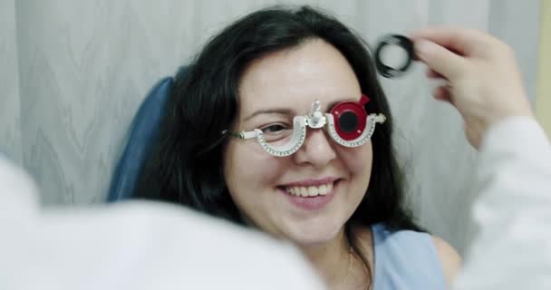Närbild synundersökning till ung kvinna med optisk phoropter, ögonläkare byter linser. Kvinna som gör ögontest — Stockvideo