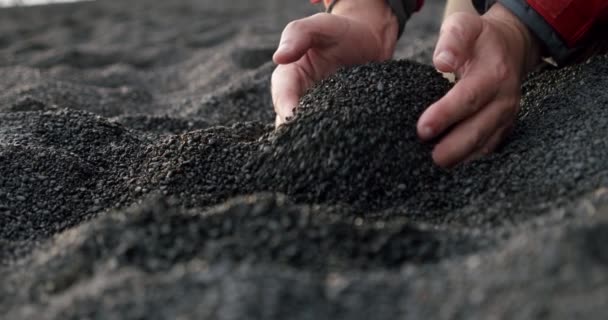 멘 사람들의 손의 느린 움직임은 검은 화산암 모래를 취하여 손가락을 통하여 레이니피라 검은 모래 해변에 부었다. V2 — 비디오