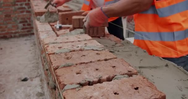 Чоловік-працівник кладе цеглу в стіну з цементом за допомогою шпателя. Крупним планом Вид зверху — стокове відео