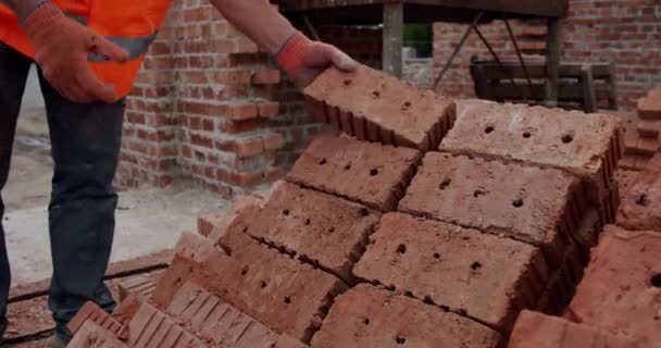 Hombre trabajador constructor toma un ladrillo en sus manos en el sitio de construcción . — Vídeos de Stock