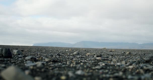 Μια κοντινή θέα ενός άνδρα πόδια σε μπότες περπάτημα σε μαύρη άμμο και πέτρες σε μια παραλία στην Ισλανδία. — Αρχείο Βίντεο