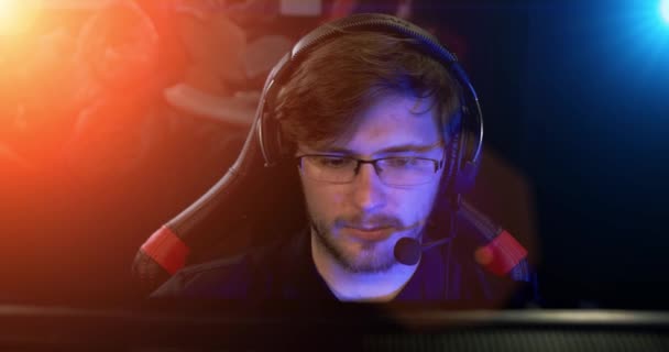 Retrato de um jogador jogando um jogo de vídeo online e comentando em um microfone, fundo com luzes de néon legais . — Vídeo de Stock