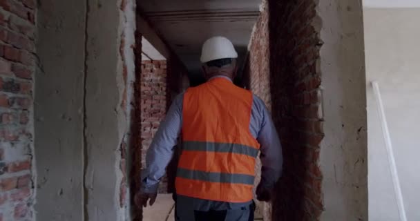 認定されていないプロの工場労働者のショットの後ハードハットウォーキング徹底的な建設を身に着けている — ストック動画